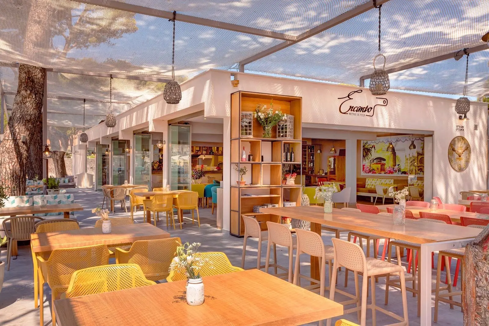Shaded terrace with colourful chairs and the ENCANTO Metros de Pizza sign
